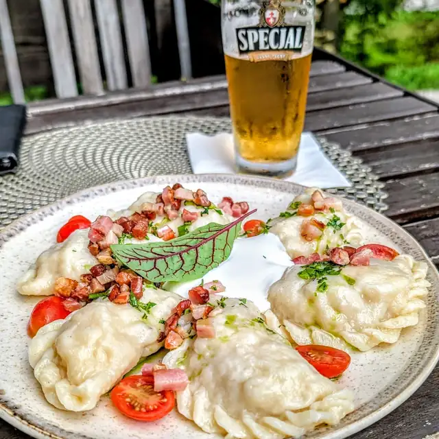 Pierogi z okrasą, śmietaną i pomidorkami na stole w ogródku, obok szklanka piwa